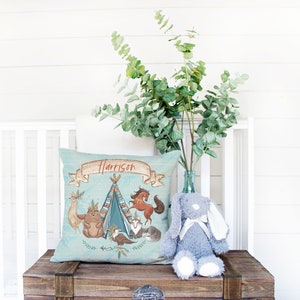 May include: A blue and white personalized pillow with a woodland animal theme. The pillow features a teepee, a horse, a fox, a bird, and a bear. The name "Harrison" is embroidered on the pillow.