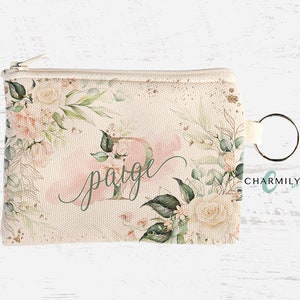 Puede incluir: Una cartera de monedas de lona rosa y blanca con un diseño floral y el nombre "Paige" escrito en cursiva. La cartera tiene una cremallera plateada y un llavero plateado.