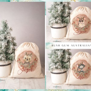 May include: Three personalized Christmas gift bags with drawstring closures. Each bag features a different Australian animal illustration with a watercolor effect. The bags are beige with red and green accents. The names "Abigail", "Brier", and "Mila" are printed on the bags.