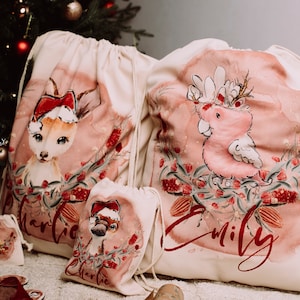 May include: Four personalized Christmas gift bags with a pink and red watercolor design. The bags feature a deer, a cockatoo, a platypus, and a duck. The bags are labeled with the names "Charlie", "Emily", "Charlie", and "Emily".