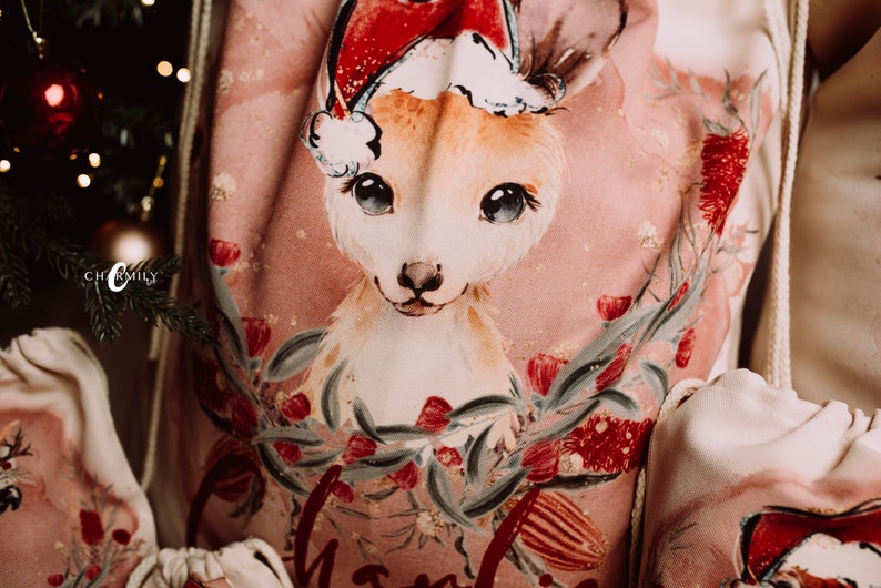 May include: A pink Christmas sack with a white drawstring. The sack features a watercolor illustration of a kangaroo wearing a Santa hat, surrounded by red and green flowers.
