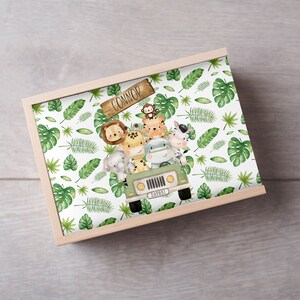 May include: A wooden box with a white background and a green jungle pattern. The box has a sign that says "Connor" and a green jeep with animals inside. The animals include a monkey, a lion, a giraffe, a hippopotamus, and a zebra.