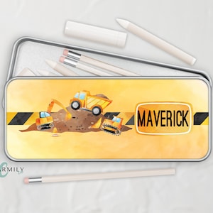 May include: A yellow metal pencil case with a watercolor design of construction vehicles on a dirt pile. The case has a black and yellow striped warning tape with the name "MAVERICK" printed on a yellow sign.
