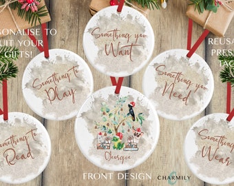 May include: Six round, white ceramic ornaments with a watercolor background. Each ornament has a different phrase printed on it in brown text. The phrases are "Something to Play", "Something to Read", "Something you Want", "Something you Need", "Something to Wear", and "Georgie".