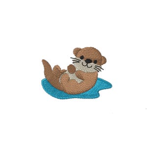 May include: An embroidered patch featuring a cartoon otter floating on its back. The otter is brown with a white belly and black whiskers. It rests on a blue water-like shape, all against a white background.