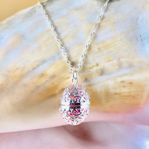 May include: A silver filigree pendant necklace with a delicate chain. The pendant is shaped like an egg and has a floral design.