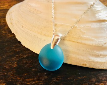 Pode incluir: Um colar de corrente de prata com um pingente de vidro do mar azul turquesa.