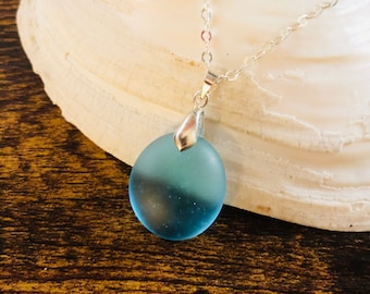Pode incluir: Um colar de corrente de prata com um pingente de vidro do mar azul claro. O pingente é redondo e tem um leve efeito degradê.