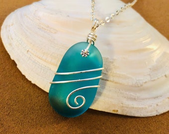May include: Teal sea glass pendant necklace with silver wire wrapping and a small silver bead accent. The pendant is hanging from a silver chain.
