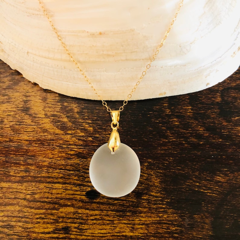 Pu&ograve; includere: Una collana con catena dorata e un ciondolo rotondo in vetro smerigliato.