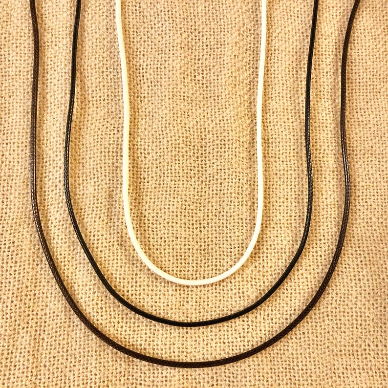 Pu&ograve; includere: Tre cordini di diversi spessori, uno bianco, uno nero e uno marrone, sono disposti su uno sfondo di tessuto beige.