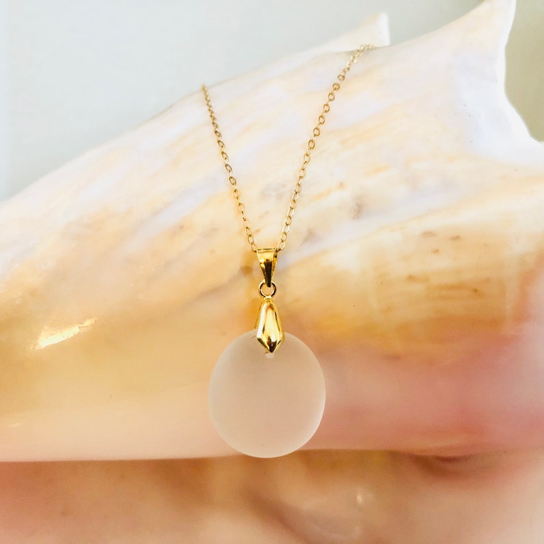 Pu&ograve; includere: Una collana con catena dorata e un ciondolo rotondo in vetro smerigliato.