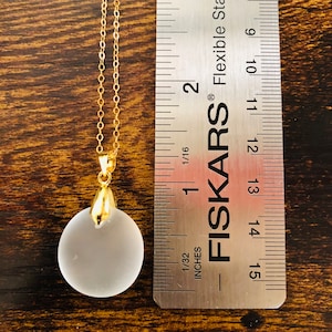Pu&ograve; includere: Una collana con catena dorata con un ciondolo in vetro smerigliato di circa 2,5 cm di diametro. Il ciondolo &egrave; rotondo e ha una superficie liscia. La collana viene misurata con un righello.
