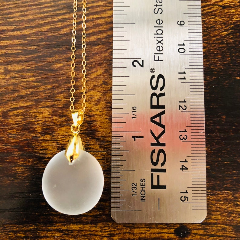 Pu&ograve; includere: Una collana con catena dorata con un ciondolo in vetro smerigliato di circa 2,5 cm di diametro. Il ciondolo &egrave; rotondo e ha una superficie liscia. La collana viene misurata con un righello.