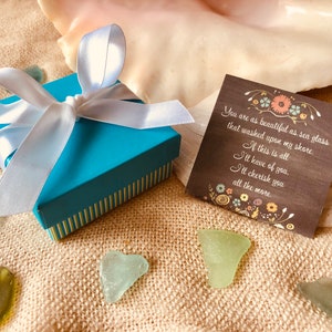 Pu&ograve; includere: Una scatola regalo blu turchese con un nastro di raso bianco e un fiocco. La scatola &egrave; appoggiata su una superficie di juta marrone con vetro di mare sparso intorno. Un piccolo biglietto con un messaggio scritto a mano &egrave; accanto alla scatola. Il messaggio dice: "Sei bella come il vetro di mare che &egrave; stato portato a riva. Se questo &egrave; tutto ci&ograve; che avr&ograve; di te, ti amer&ograve; ancora di pi&ugrave;."