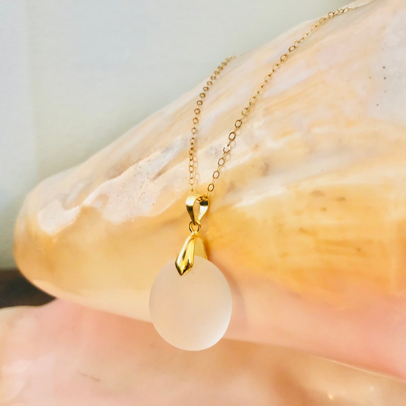 Pu&ograve; includere: Una collana con catena dorata e un ciondolo in vetro bianco smerigliato. Il ciondolo &egrave; rotondo e ha un'anellina in oro.