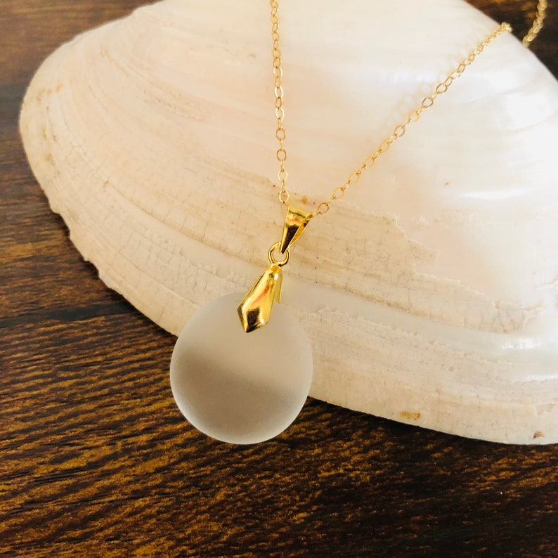 Pu&ograve; includere: Una collana con catena dorata e un ciondolo rotondo in vetro smerigliato.