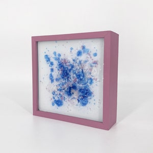 Peut inclure: Une œuvre d'art encadrée avec un fond blanc et des éclaboussures de peinture bleue et rose. Le cadre est de couleur rose clair.