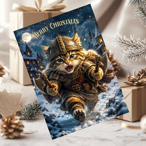 May include: A rectangular greeting card featuring a brown tabby cat dressed in detailed bronze-colored Viking armor and a horned helmet, holding two small axes. The cat is running through a snowy landscape with a village and full moon. Text reads Merry Christmas.