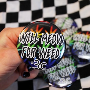 May include: A collection of round, black buttons with the text "WILL MEOW FOR WEED" in white, with a rainbow cannabis leaf design. The buttons are on a black and white checkered background.
