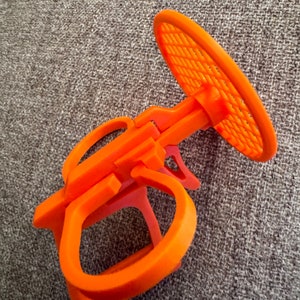 May include: Orange plastic bike rack with a circular, mesh-like top. The rack is designed to hold a bike wheel.