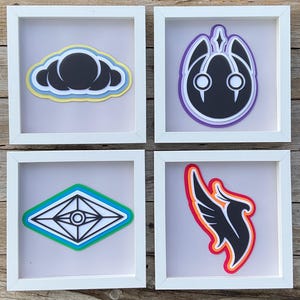 May include: Four framed art pieces with layered paper designs. The designs include a cloud, a stylized face, a geometric eye, and a wing. Each design is in a white square frame.