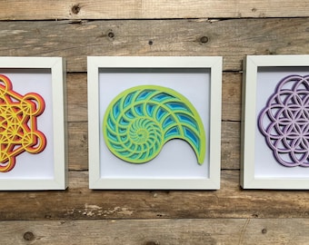 May include: Three framed geometric art prints with white frames. The first print features a yellow, orange, and red geometric design. The second print features a green and blue spiral design. The third print features a purple geometric design.