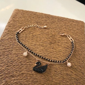May include: A delicate gold chain bracelet with a black crystal swan pendant and two small black crystal ball charms.