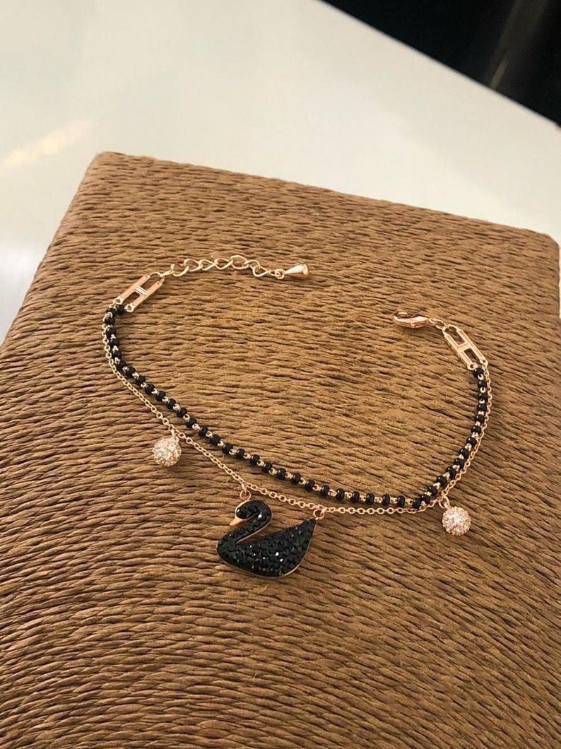 May include: A delicate gold chain bracelet with a black crystal swan pendant and two small black crystal ball charms.