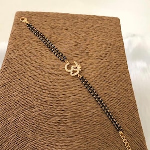 May include: A gold Om charm bracelet with black beads. The charm is decorated with clear sparkling stones.