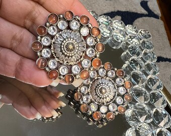 May include: A pair of silver earrings with a circular design. The earrings are adorned with clear and brown stones.