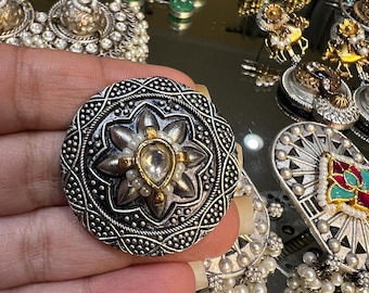 May include: A silver and gold ring with a large, clear stone in the center. The ring is decorated with intricate designs and small white pearls.