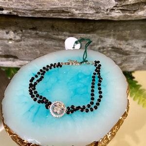 May include: A black beaded bracelet with a large, clear, round gemstone in a gold setting.