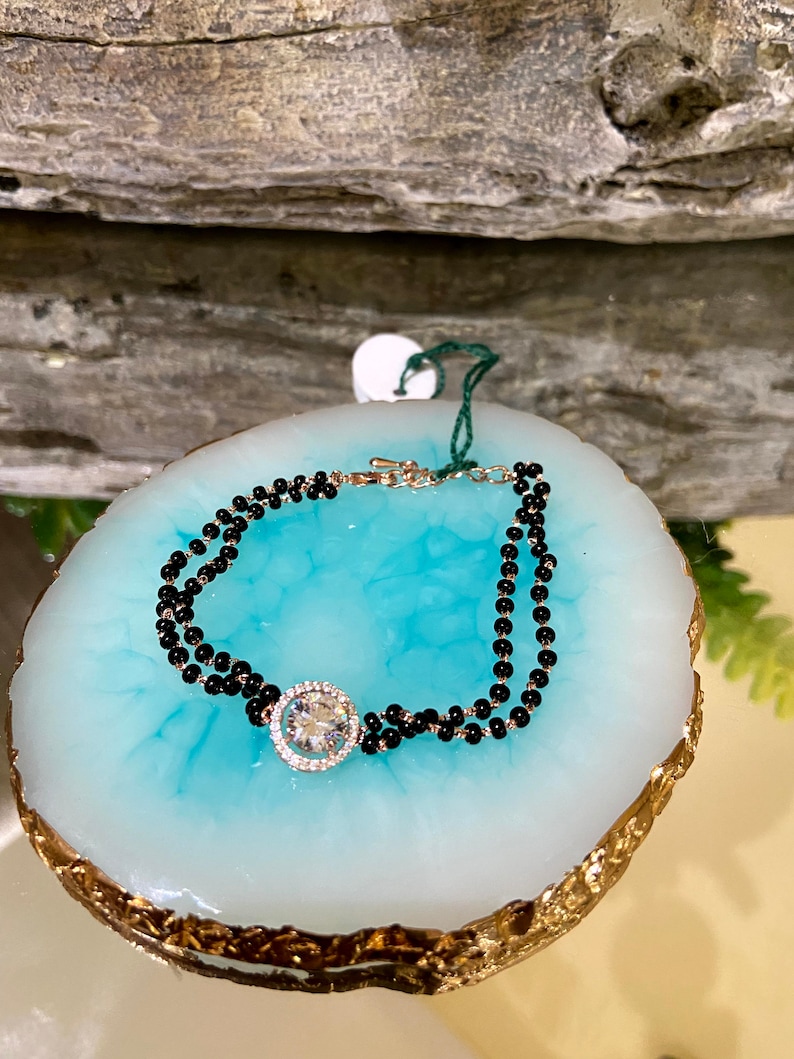 May include: A black beaded bracelet with a large, clear, round gemstone in a gold setting.