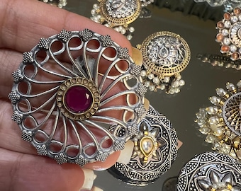 May include: A silver and gold filigree earring with a pink gemstone in the center. The earring is surrounded by other similar earrings in the background.