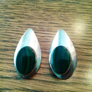 May include: A pair of silver earrings with green malachite stones. The earrings are oval shaped and have a smooth, polished finish.