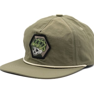 Puede incluir: Una gorra de béisbol verde y blanca con un parche de calavera con un casco de camuflaje.