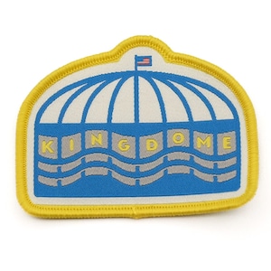 Pode incluir: Um remendo bordado amarelo e azul com um edifício branco com uma cúpula e a palavra "KINGDOME" em letras amarelas.