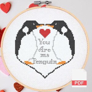 May include: Cross-stitch hoop art featuring two penguins facing each other, forming a heart shape with a red heart in the center. The text "You Are my Penguin" is stitched below. The design is set in a wooden hoop.