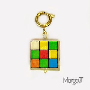 May include: A gold-colored charm featuring a miniature Rubik's Cube design. The cube has colorful squares in red, yellow, green, blue, and orange. The charm is attached to a gold-colored clasp. The text "MargotT" is in the bottom right corner.