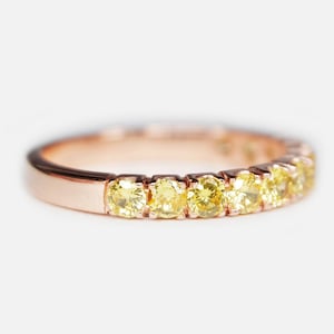 May include: A rose gold band ring with a row of small, round, yellow gemstones.