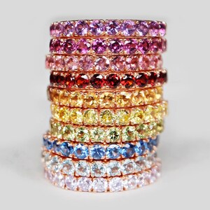 May include: A stack of colourful gemstone rings in a rainbow pattern. The rings are made of rose gold and feature a variety of gemstones, including amethyst, pink sapphire, ruby, citrine, peridot, blue topaz, aquamarine, and rose quartz.