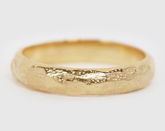 May include: A gold band ring with a textured, hammered finish. The ring is a simple design with a smooth, rounded edge.