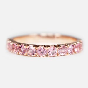 May include: A delicate rose gold band ring with a row of pink gemstones.