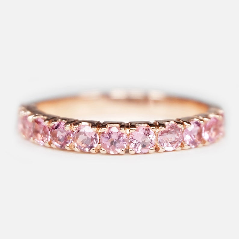 May include: A delicate rose gold band ring with a row of pink gemstones.