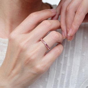 May include: A delicate eternity band ring with a row of pink gemstones set in a gold band.