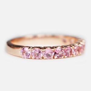 May include: A delicate rose gold band ring with a row of pink gemstones.