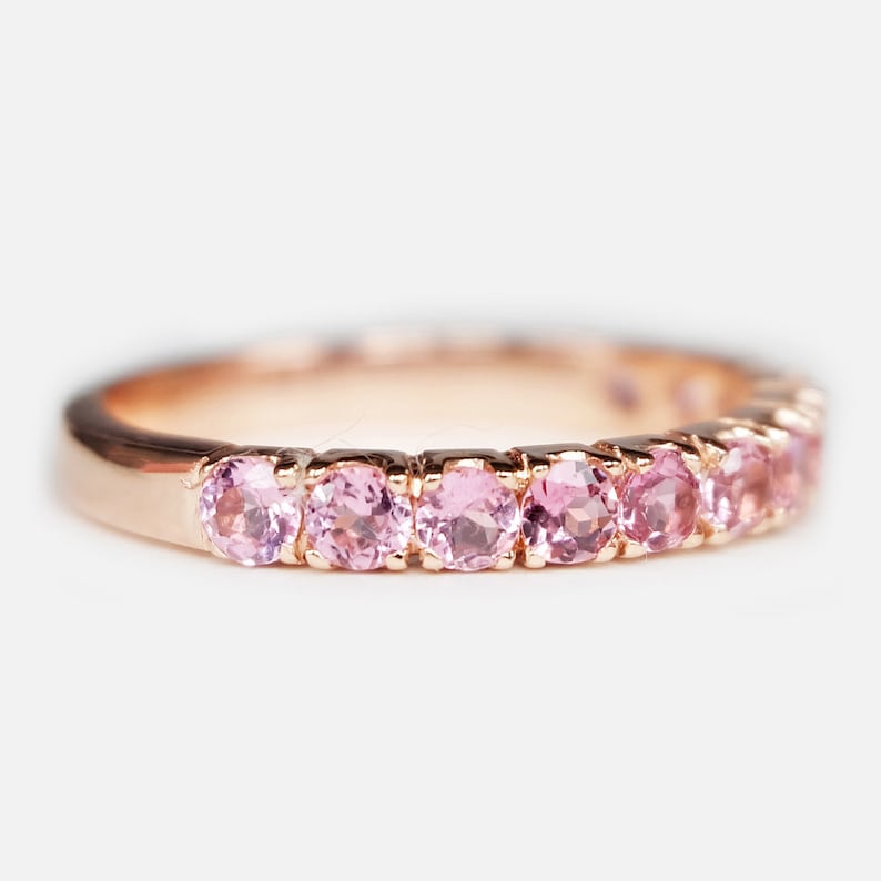 May include: A delicate rose gold band ring with a row of pink gemstones.