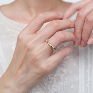 May include: A gold band ring with a textured design. The ring is worn on a person's finger.