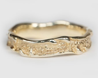 May include: A gold band ring with a textured, organic design. The band is thick and has a wavy, irregular shape.